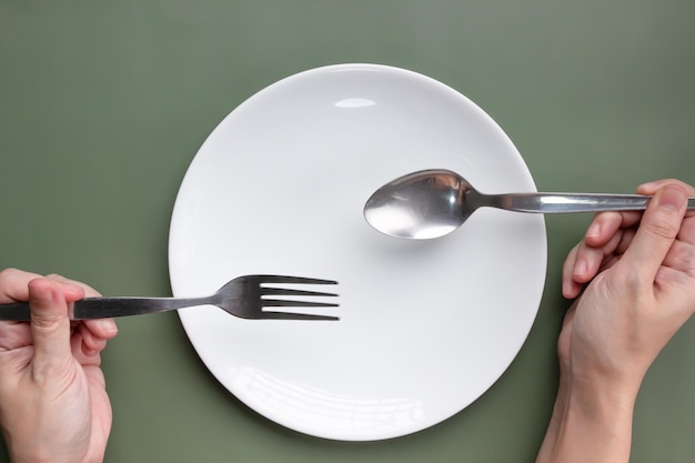 Mano de mujer sosteniendo cuchara y tenedor con plato blanco que lee para comer para el desayuno, el almuerzo y la cena