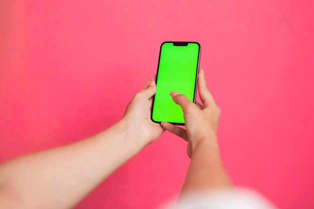 Mano de mujer sosteniendo un desplazamiento de teléfono inteligente de pantalla verde y pantalla táctil sobre fondo rosa.