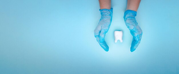 Mano de mujer sosteniendo diente blanco sobre fondo azul pastel Concepto médico de estomatología de dentista