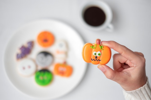 Mano de mujer sosteniendo una divertida galleta de Halloween durante el consumo de café. Feliz día de Halloween, truco o amenaza, hola octubre, otoño otoño, concepto tradicional, fiesta y vacaciones