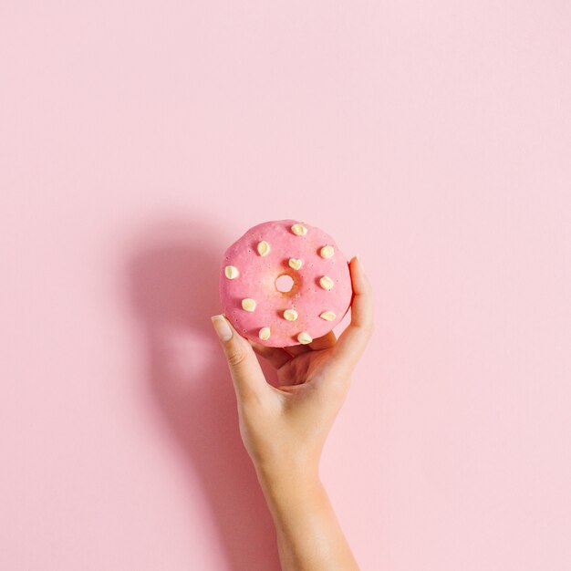 Mano de mujer sosteniendo donut en rosa