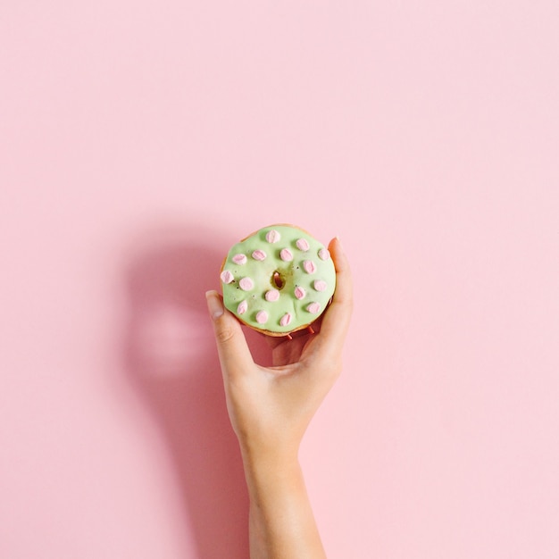 Foto mano de mujer sosteniendo donut sobre fondo rosa.