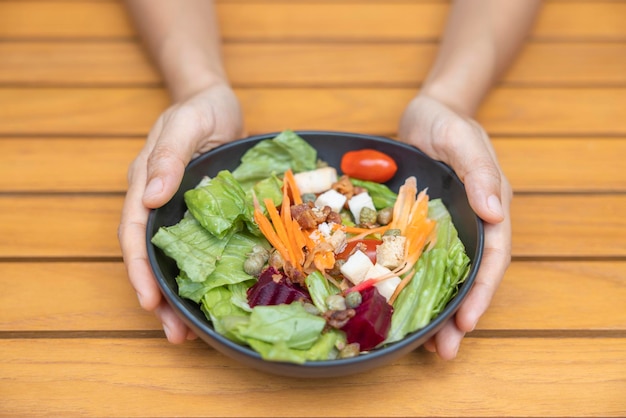 Mano de mujer sosteniendo ensalada de verduras y desayunando