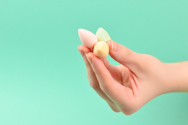 Mano de mujer sosteniendo esponja de belleza sobre fondo verde