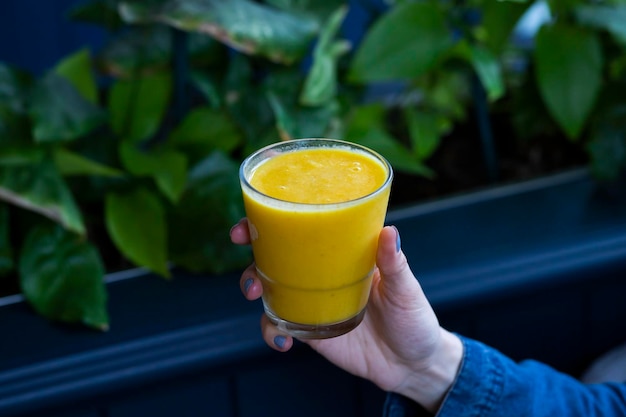 Mano de mujer sosteniendo un frasco de vidrio de batido de naranja, jugo fresco sobre fondo azul. bebida saludable