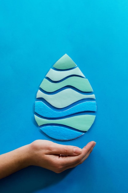 Foto mano de mujer sosteniendo una gota de agua cortada en papel sobre fondo azul agua limpia y saneamiento ahorrando agua concepto de ecología del día mundial del agua