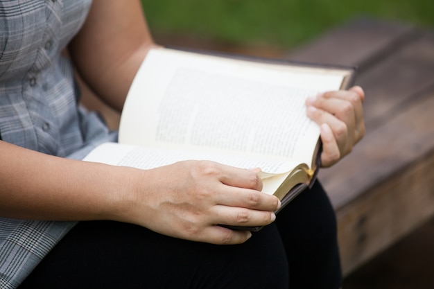 Mano de mujer sosteniendo y leyendo un libro en el parque natural