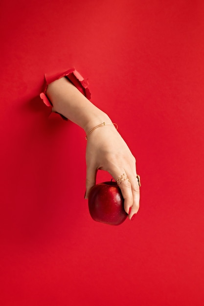 Mano de mujer sosteniendo manzana roja a través del agujero en la pared de papel rojo