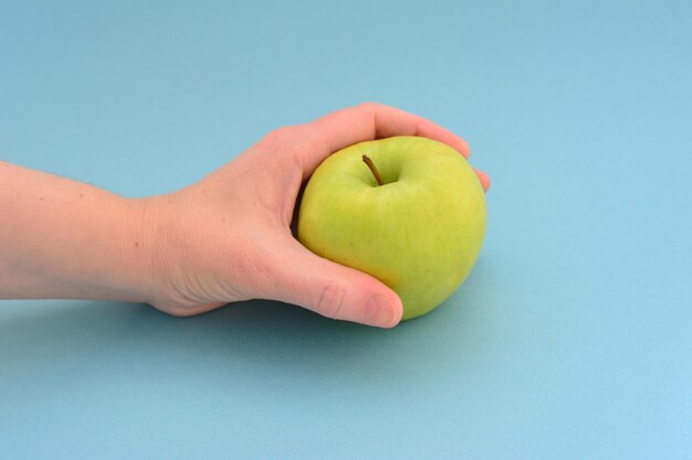 mano de mujer sosteniendo manzana verde en el fondo azul aislado, primer plano