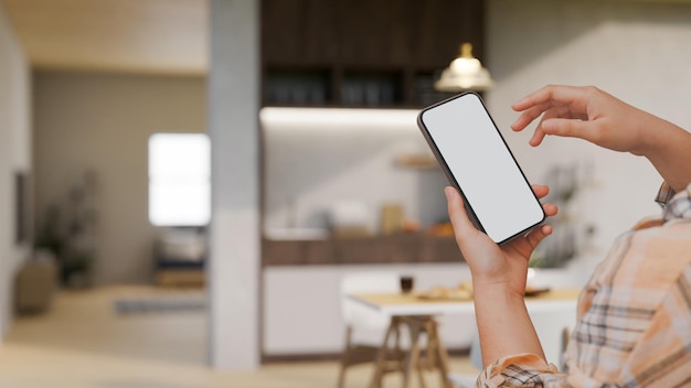 La mano de una mujer sosteniendo una maqueta de teléfono inteligente sobre un comedor casero minimalista y moderno y borroso