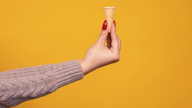 Mano de mujer sosteniendo pequeño cono de helado crujiente en blanco aislado