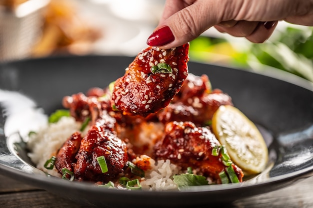 Mano de mujer sosteniendo un pollo picante glaseado pegajoso con semillas de sésamo con un plato con arroz