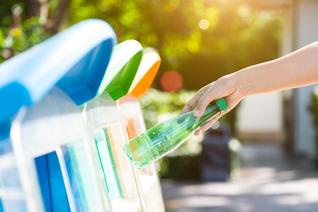 Mano de mujer sosteniendo y poniendo residuos de botellas de plástico en la basura