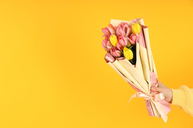 Mano de mujer sosteniendo un ramo de flores sobre un fondo amarillo