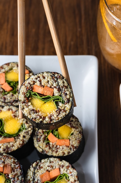 Mano de mujer sosteniendo rollo de sushi vegano con palillos de madera