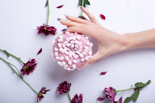 Mano de mujer sosteniendo una rosquilla rosa