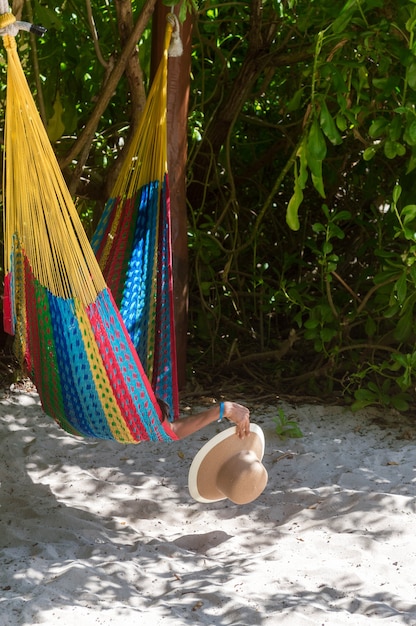 Mano de mujer sosteniendo el sombrero de una hamaca cerca de la playa