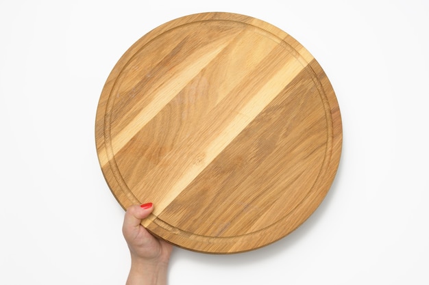 Mano de mujer sosteniendo la tabla de pizza de madera redonda vacía en la mano, parte del cuerpo sobre fondo blanco.