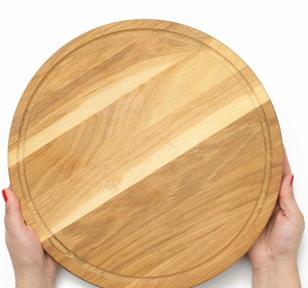 Mano de mujer sosteniendo la tabla de pizza de madera redonda vacía en la mano, parte del cuerpo sobre fondo blanco.