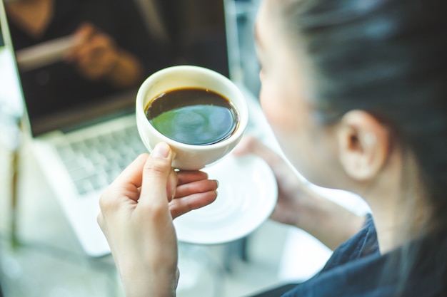 Mano de mujer sosteniendo una taza de café caliente en el escritorio de oficina