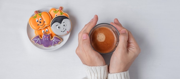 Mano de mujer sosteniendo la taza de café durante comer divertidas galletas de Halloween. Feliz día de Halloween, truco o amenaza, hola octubre, otoño otoño, concepto tradicional, fiesta y vacaciones