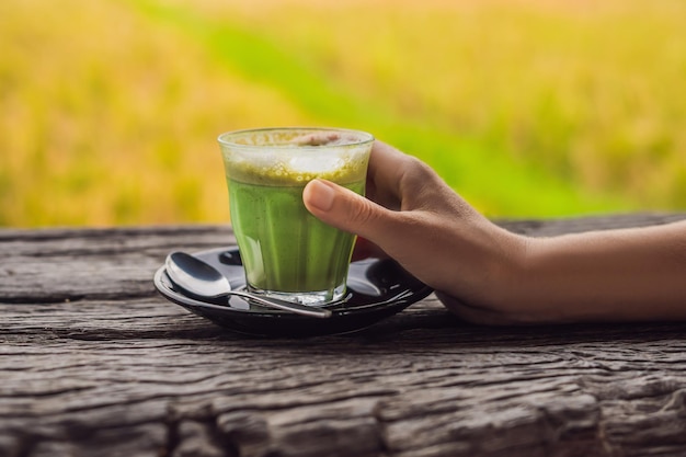 Mano de mujer sosteniendo una taza de matcha Latte, té verde, en la vieja mesa de fondo de madera.