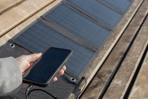 Mano de mujer sosteniendo un teléfono conectado a un panel solar