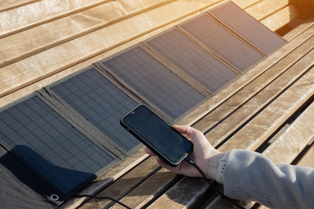 Mano de mujer sosteniendo un teléfono conectado a un panel solar