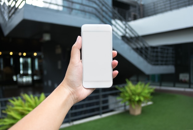 mano de mujer sosteniendo teléfono inteligente móvil de pantalla en blanco con fondo borroso