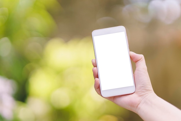 Mano de mujer sosteniendo un teléfono inteligente con pantalla blanca en blanco para enviar mensajes de texto en un fondo borroso