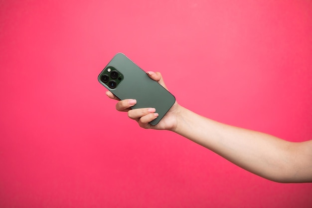 Mano de mujer sosteniendo un teléfono inteligente verde sobre fondo rosa.
