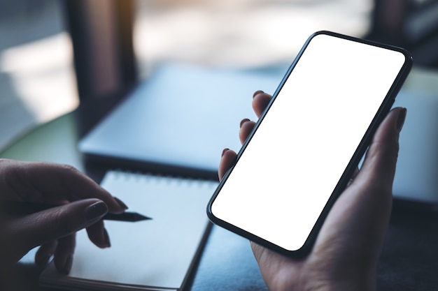 una mano de mujer sosteniendo teléfono móvil negro con pantalla de escritorio en blanco