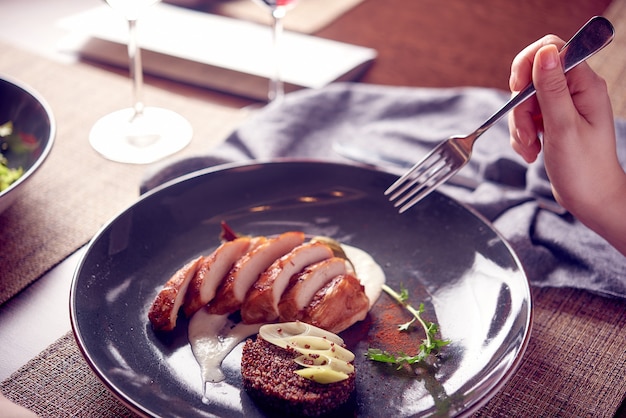 Mano de mujer sosteniendo tenedor comiendo carne de pechuga de pollo en restaurante de lujo