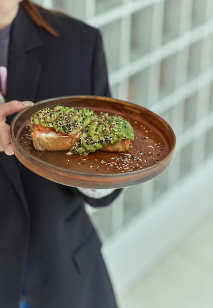 La mano de la mujer sosteniendo una tostada de aguacate saludable, un aguacate maduro, pan de grano entero, sésamo, semillas de lino, dieta ceto vegana, estilo de vida saludable, guacamole vegetariano de moda.