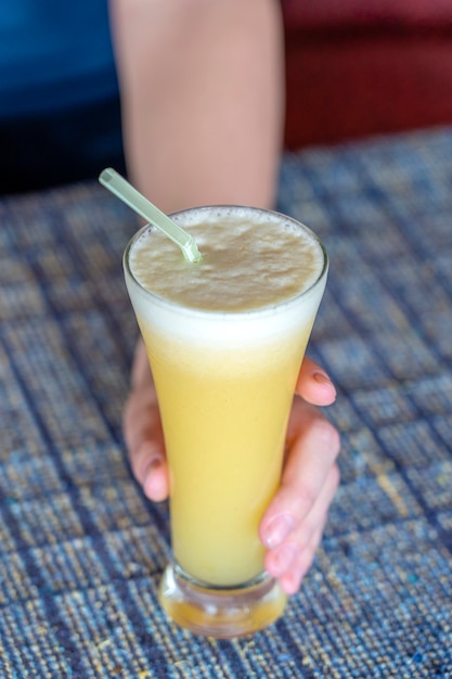 Mano de mujer sosteniendo un vaso de jugo de piña fresco, de cerca, concepto de estilo de vida saludable