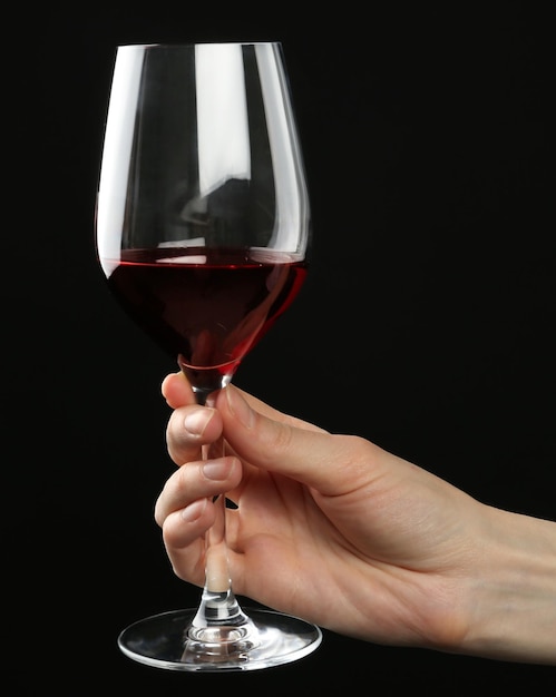 Foto la mano de la mujer sosteniendo un vaso de vino tinto sobre un fondo negro