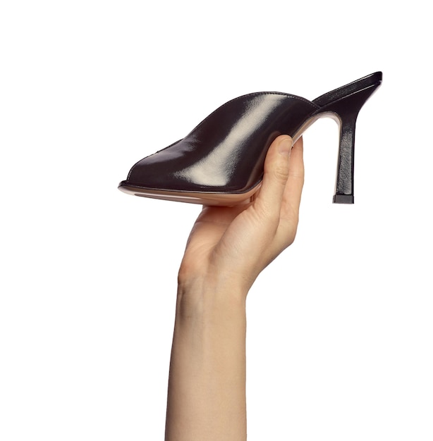 La mano de una mujer sosteniendo un zapatillo de verano de tacón alto negro de moda aislado sobre un fondo blanco Presentación de zapatos elegantes en la mano