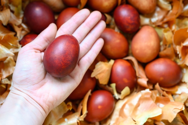 Mano de mujer sostiene cáscaras de cebolla pintadas con huevo de Pascua