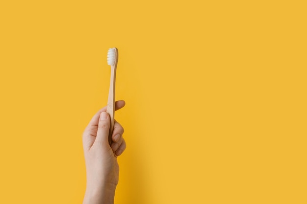 La mano de una mujer sostiene un cepillo de dientes de madera Concepto Productos para el cuidado natural