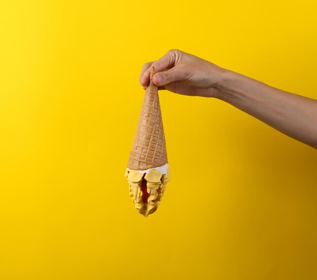 La mano de la mujer sostiene un cono de crema sobre un fondo amarillo Fondo de verano