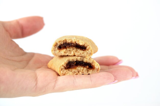 La mano de una mujer sostiene una galleta rota con un relleno de frutas sobre un fondo blanco.