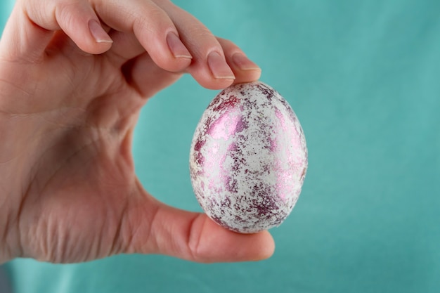 La mano de una mujer sostiene un huevo de Pascua brillante decorado a la moda