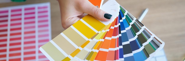La mano de la mujer sostiene muestras de color sobre su escritorio, el diseñador gráfico elige el color de la muestra para