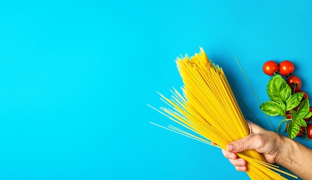 Mano de mujer sostiene pasta cerca de tomates y hojas de albahaca