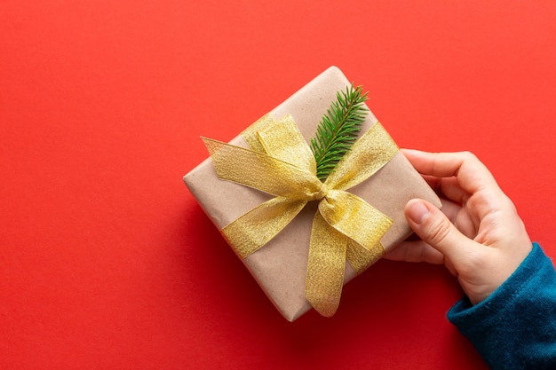 Mano de mujer sostiene un presente decorado en estilo minimalista en rojo