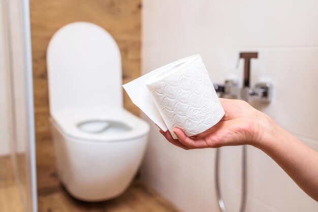 La mano de una mujer sostiene un rollo de papel higiénico blanco de cerca Fondo de baño