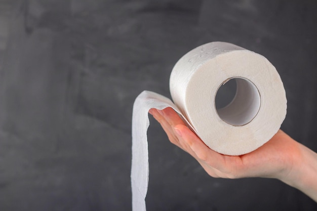 La mano de una mujer sostiene un rollo de papel higiénico sobre un fondo gris