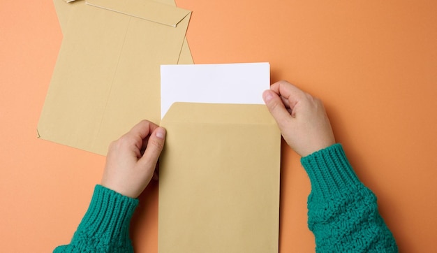la mano de la mujer sostiene sobres de papel en un fondo naranja vista superior Correspondencia