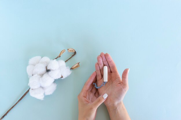 La mano de la mujer sostiene un tampón sanitario con el algodón al lado.