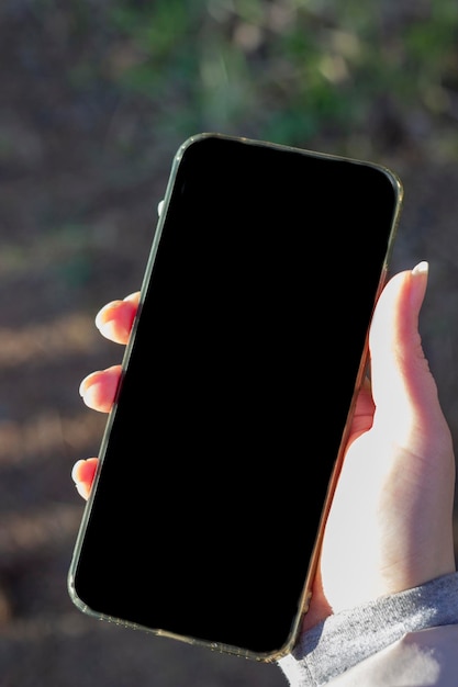 Foto la mano de una mujer sostiene un teléfono con una pantalla negra teléfono en mano con un lugar para anunciar